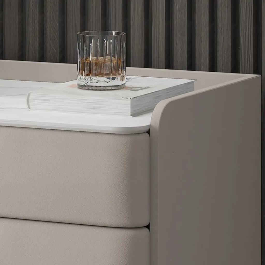 Table de chevet moderne à 3 tiroirs avec plateau en pierre, finitions dorées et revêtement en cuir.