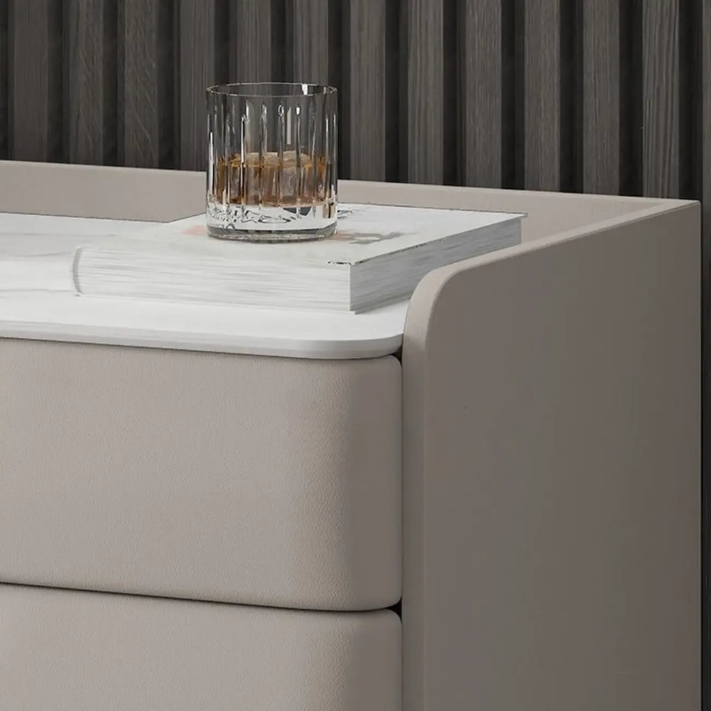 Table de chevet moderne à 3 tiroirs avec plateau en pierre, finitions dorées et revêtement en cuir.